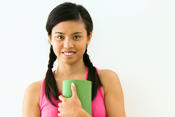 Smiling young woman holding yoga mat.