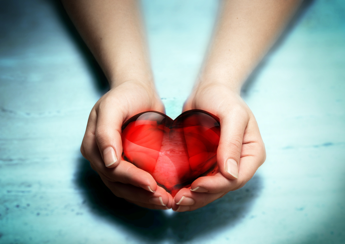 cuped hands holding a dark red see-through glass heart over a light blue background