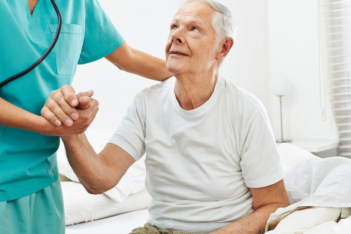 An older man being asissted out of bed by a nurse