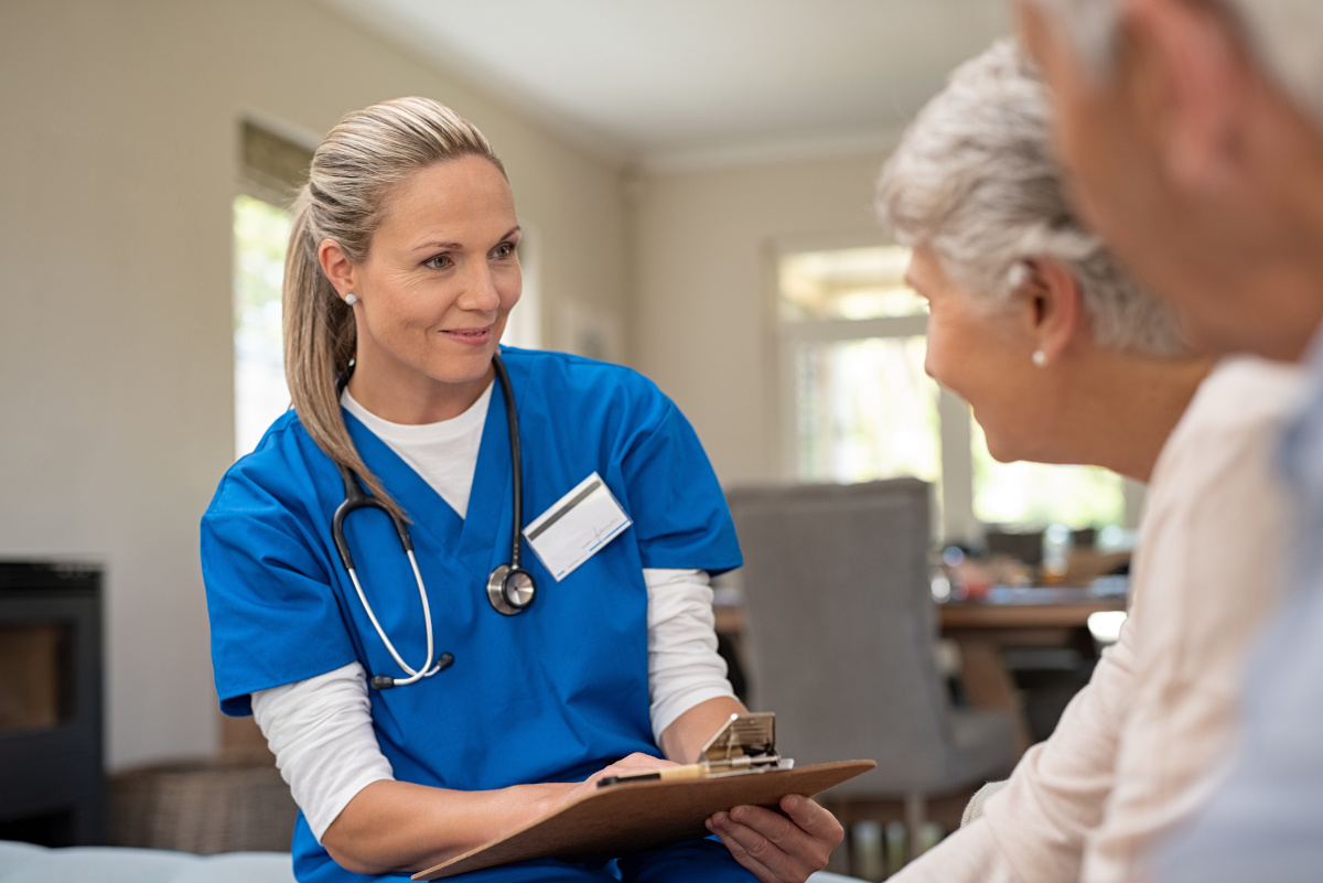 An older nurse talking to two senior citizens while taking notes on a clipboard